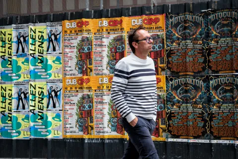Homme au pull rayé passant devant une série d'affiches